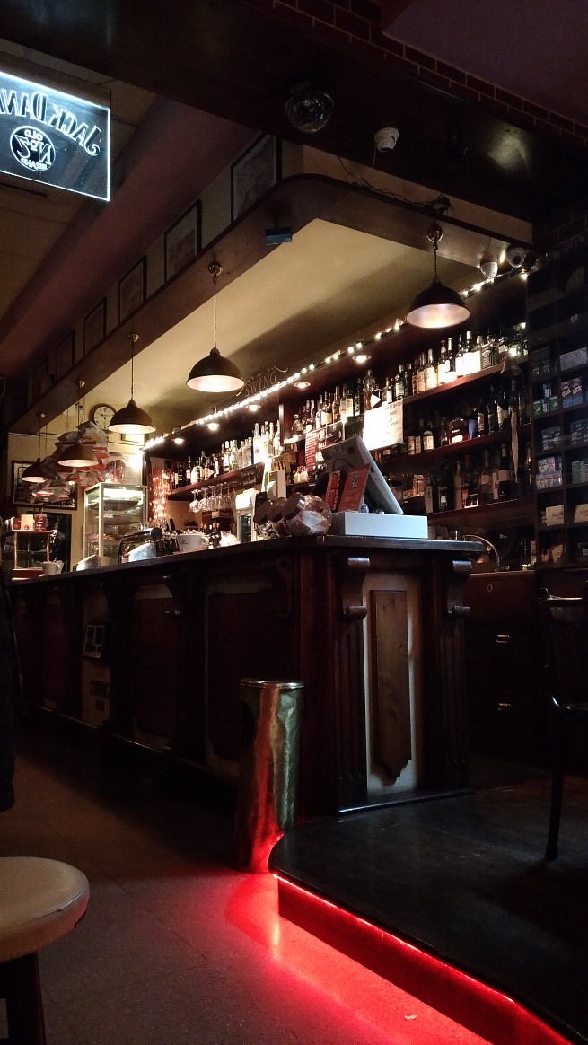 Il bancone storico dello Swing Pub con bottiglie, legno scuro e luci vintage